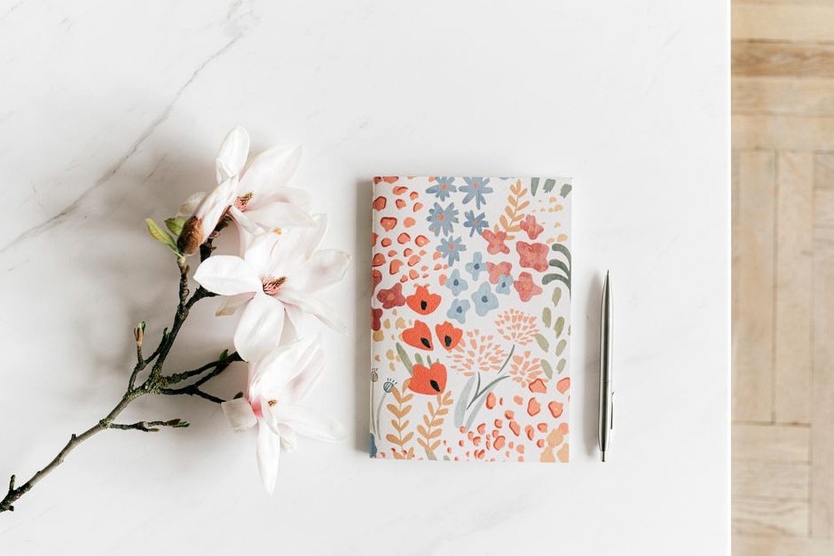 Floral notebook, pen and pale flowers arranged on a light desk.