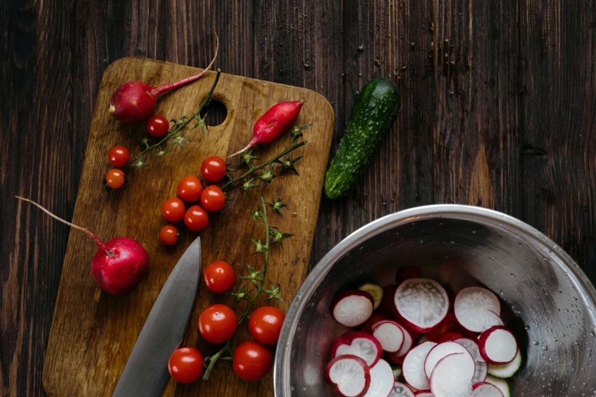 Fresh tomatoes, radishes and cucumber arranged on a dark wooden table.